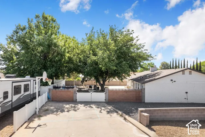 Paved driveway with basketball hoop, white privacy fencing, and mature trees