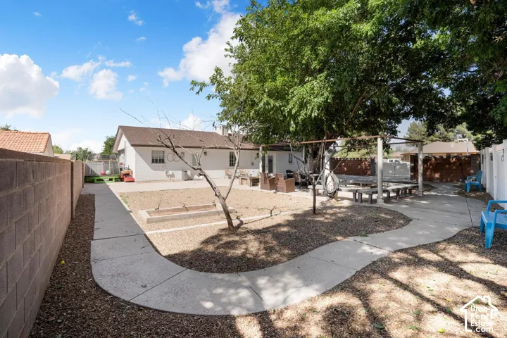 Expansive backyard featuring a concrete pathway, gravel ground cover, a shaded patio structure, and a perimeter fence