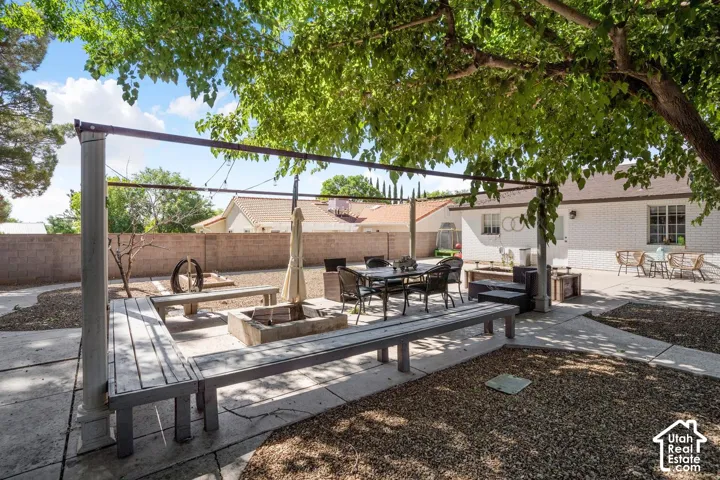Outdoor patio area featuring a built-in fire pit with surrounding benches, a separate paved dining space, and a mature shade tree