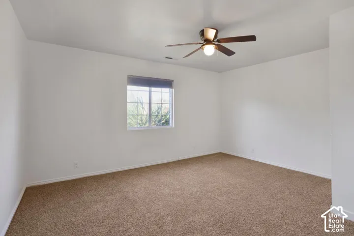 Spacious room featuring neutral carpeting, a large window with blinds, and a ceiling fan with integrated lighting