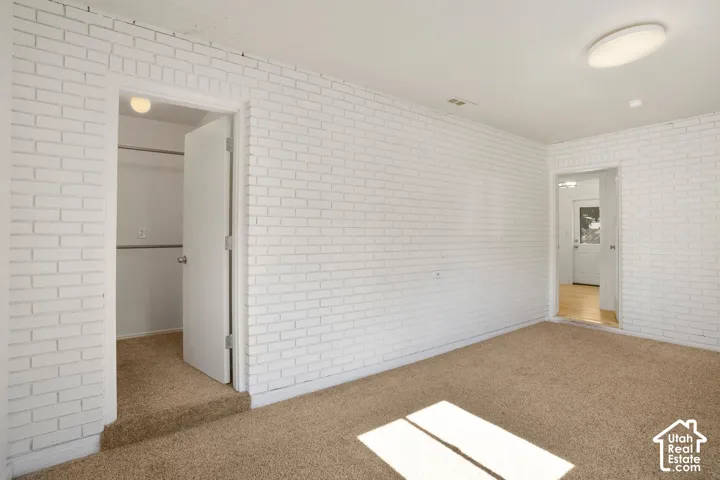 White painted brick walls throughout, carpeted flooring, and a flush mount ceiling light fixture