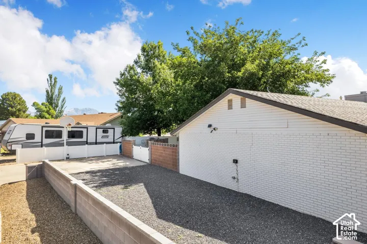 White brick exterior with a gable roof, gravel ground cover, concrete block retaining walls, and a white vinyl fence