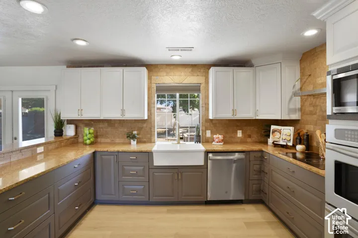 Kitchen featuring two-tone cabinetry, light-toned wood-finish flooring, recessed lighting, and a farmhouse sink