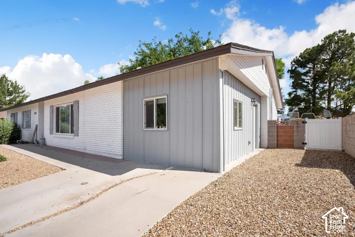 White painted brick exterior with gray vertical siding, concrete driveway, gravel landscaping, and a white privacy gate