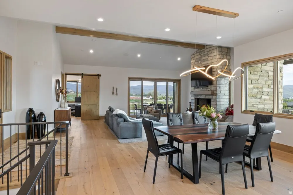 Open-concept living space featuring wood-finish flooring, a stone-clad fireplace, and a contemporary linear chandelier