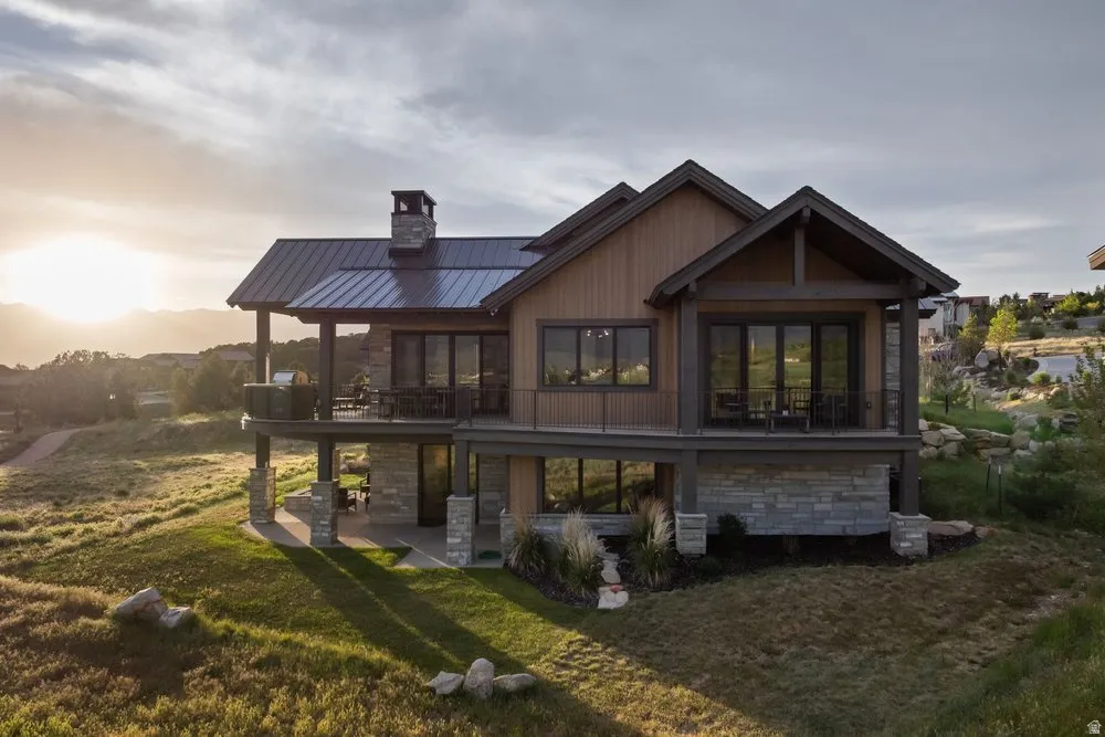 Architectural residence featuring a metal roof, stone and wood siding, multiple balconies, and an outdoor patio