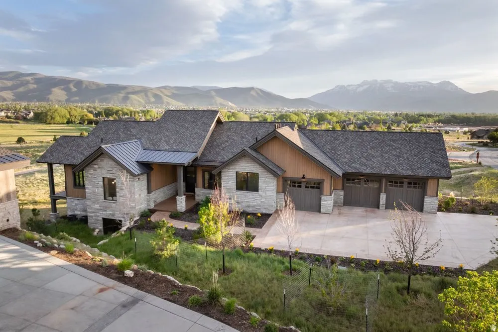Stone and wood-sided exterior featuring a multi-car garage, covered entry, and asphalt shingle roofing