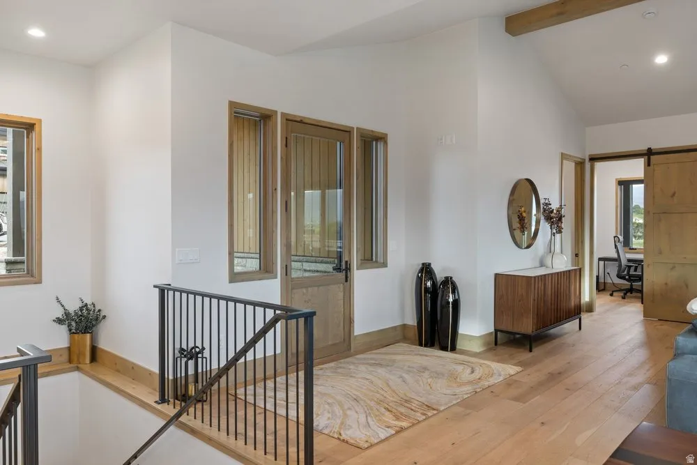 Entryway with light wood-finish flooring, white walls, and exposed ceiling beam