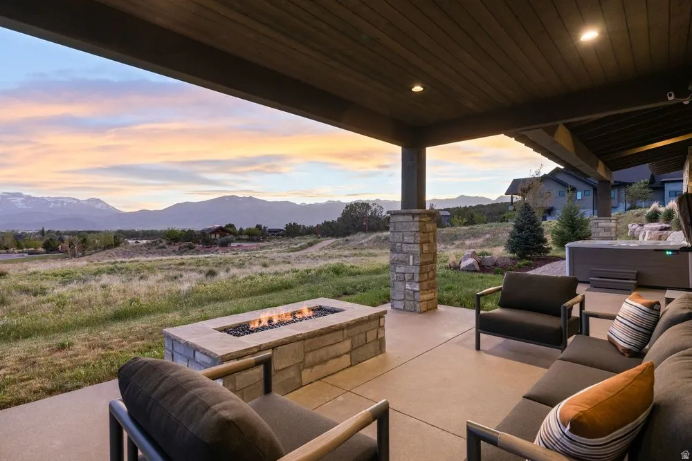 Expansive covered patio featuring a stone-clad fire pit, concrete flooring, and a hot tub