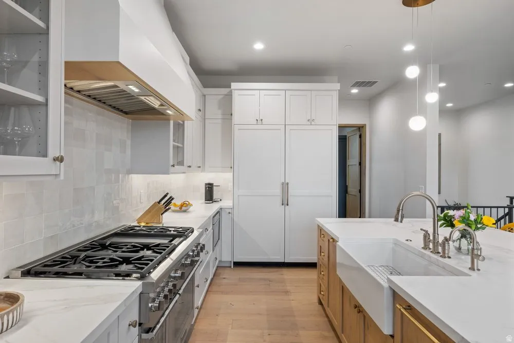 Modern kitchen featuring a large range with a custom hood, light wood-finish flooring, and white cabinetry