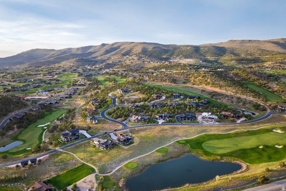 Expansive residential community featuring a golf course, multiple water features, curvilinear roadways, and mature landscaping set against a mountainous backdrop