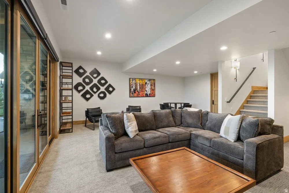 Spacious lower-level living area with recessed lighting, light-toned carpet flooring, and a stone exterior visible through extensive sliding glass doors