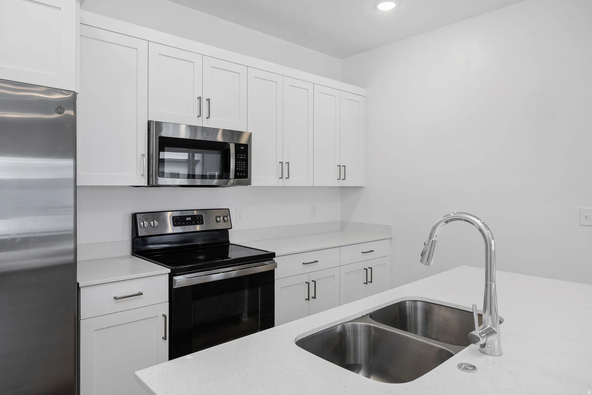 Kitchen featuring white shaker cabinetry, stainless steel appliances, light-toned countertops, a dual basin stainless steel sink, and a chrome pull-down faucet