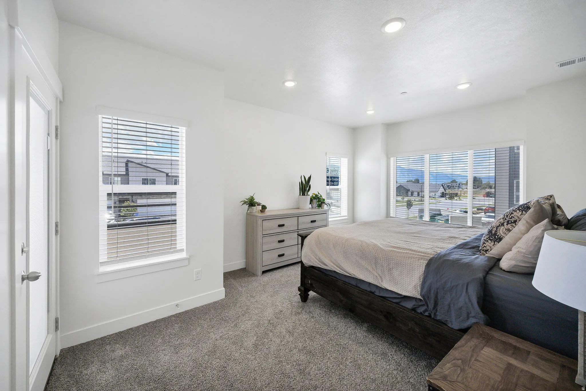 Bright bedroom featuring multiple windows with blinds, recessed lighting, white walls, and gray carpeting