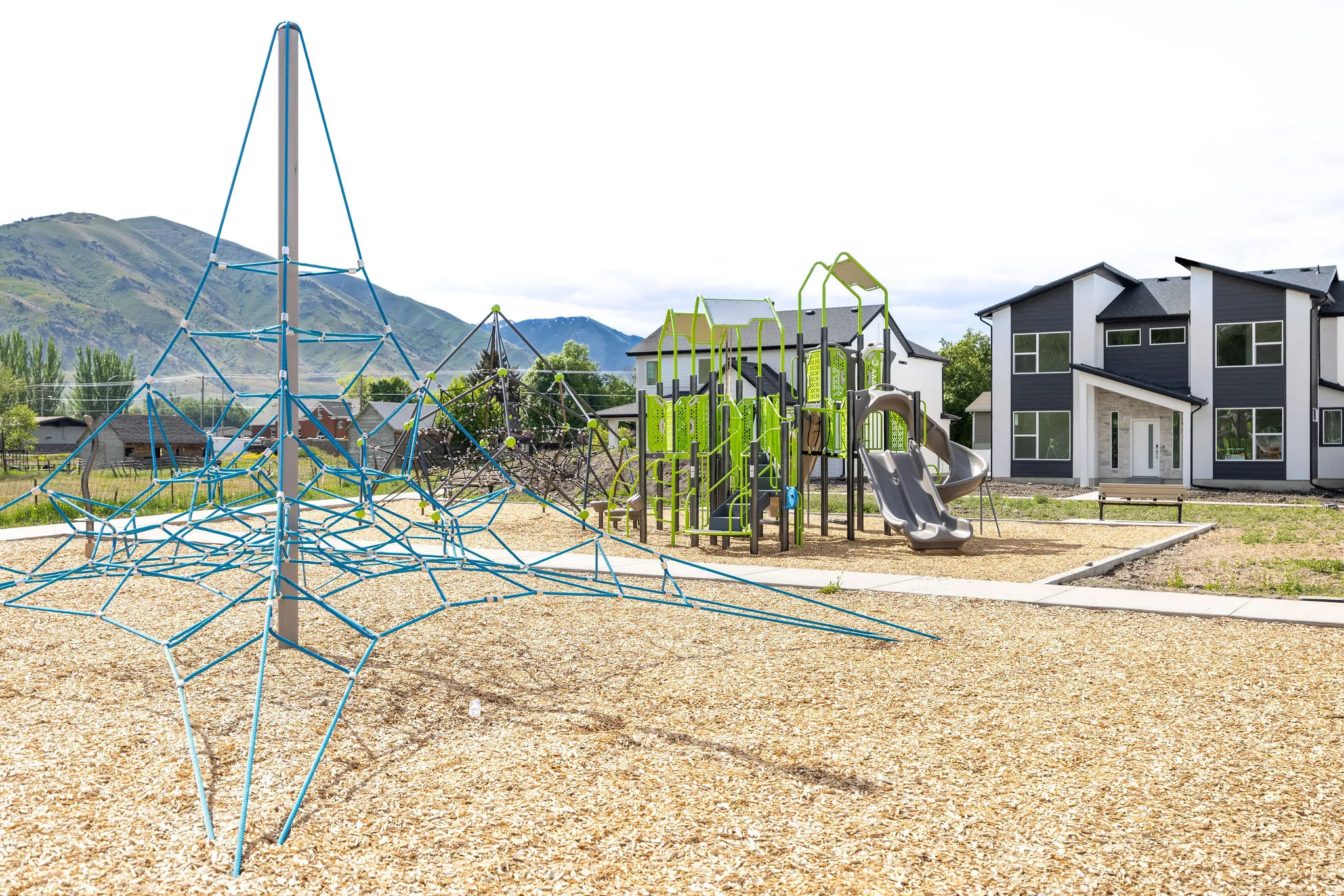 Community playground featuring a rope climbing structure, slide, and wood chip ground cover