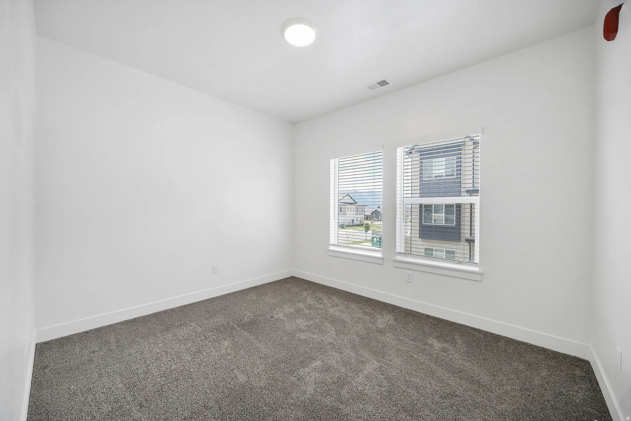 Carpeted room featuring white walls, white baseboards, two windows with blinds, and an overhead recessed light fixture