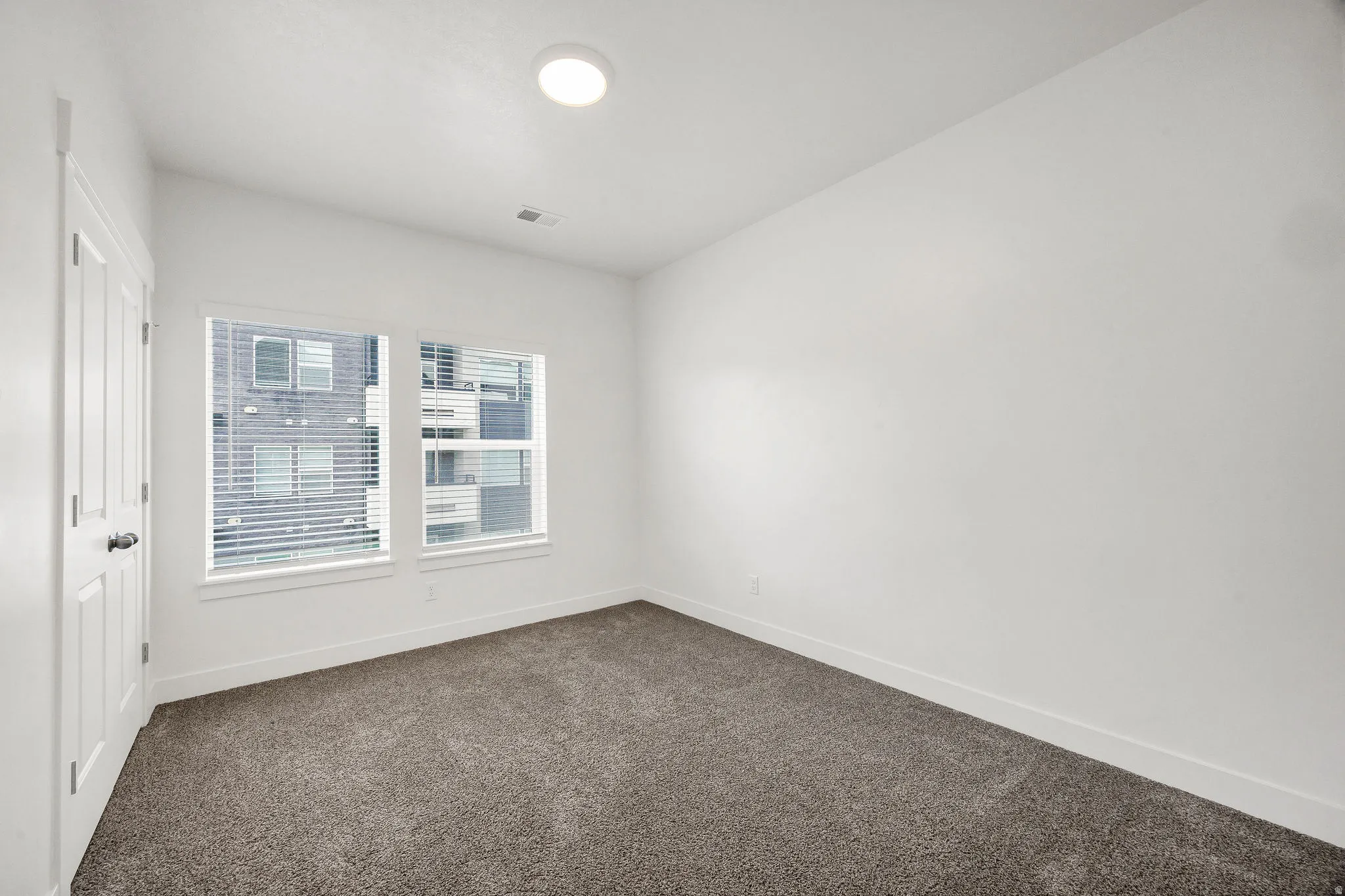 Room featuring plush gray carpet, white walls, and a white ceiling with a flush-mount circular light fixture
