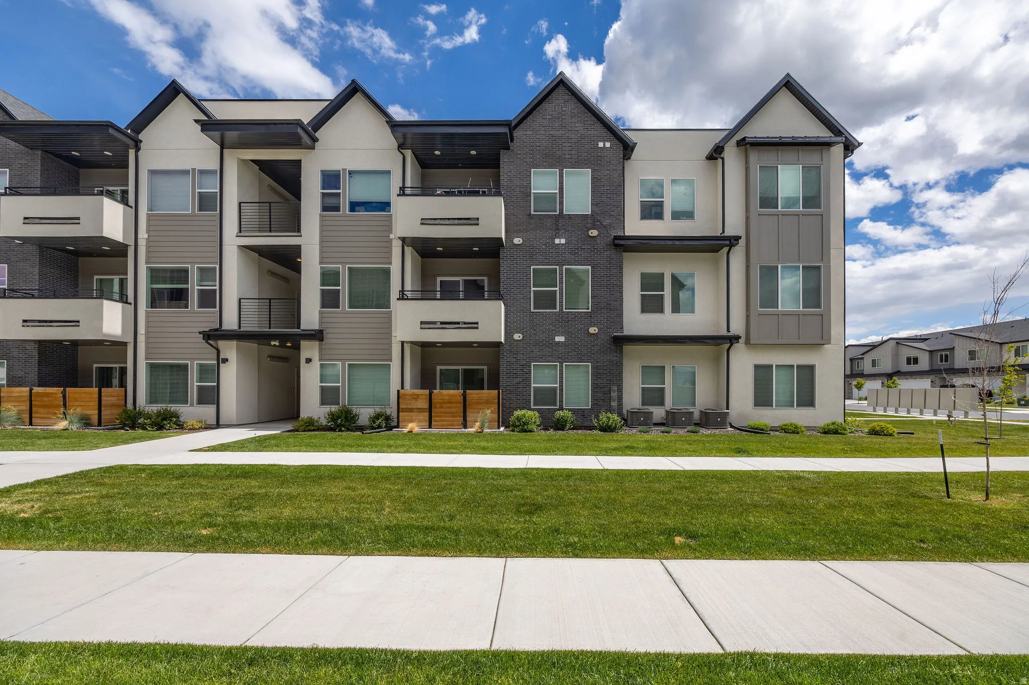 Modern multi-story building featuring light stucco, horizontal siding, and dark brick facades