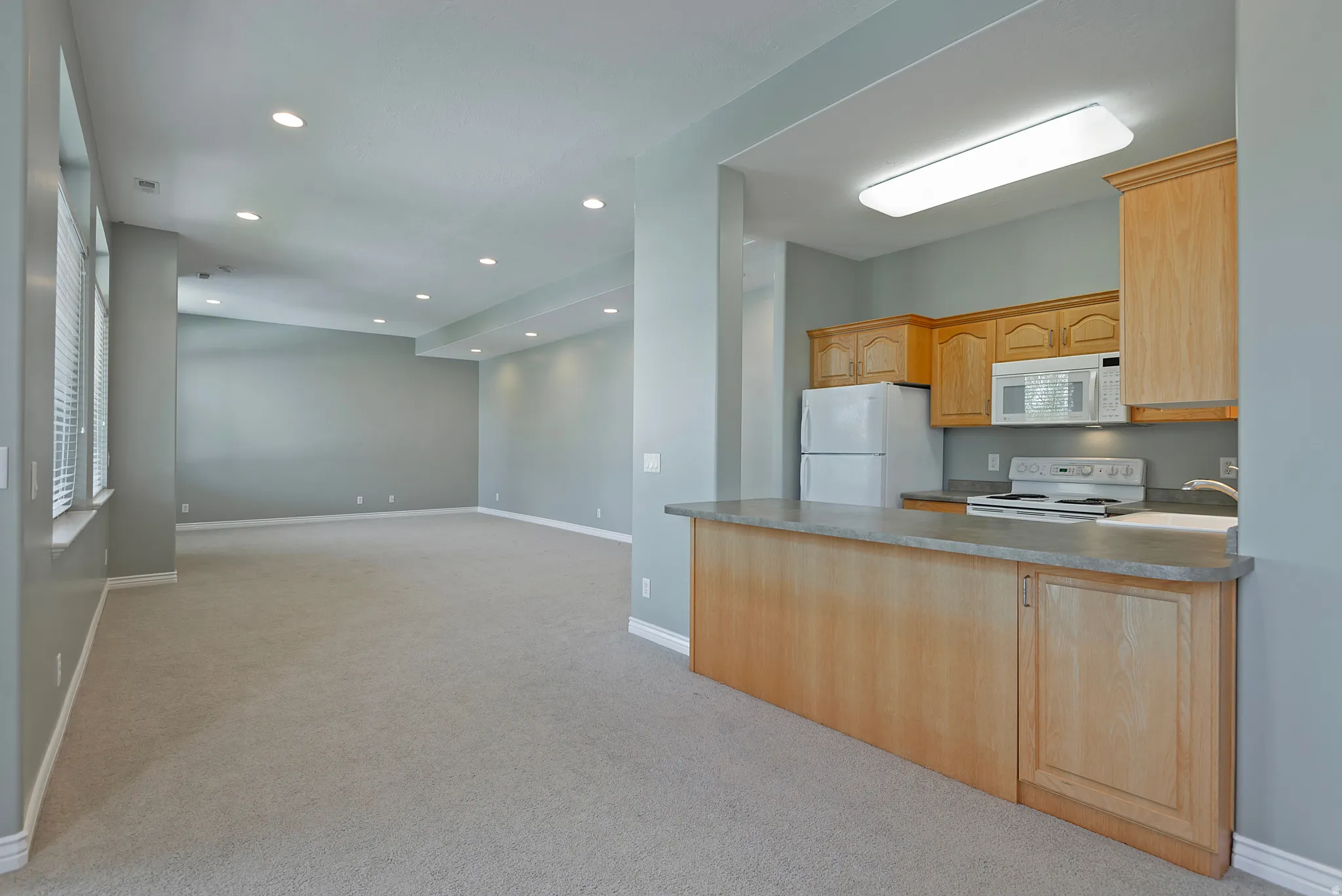 Open-concept living space featuring a kitchen with wood cabinetry, a built-in microwave, white appliances, and a breakfast bar