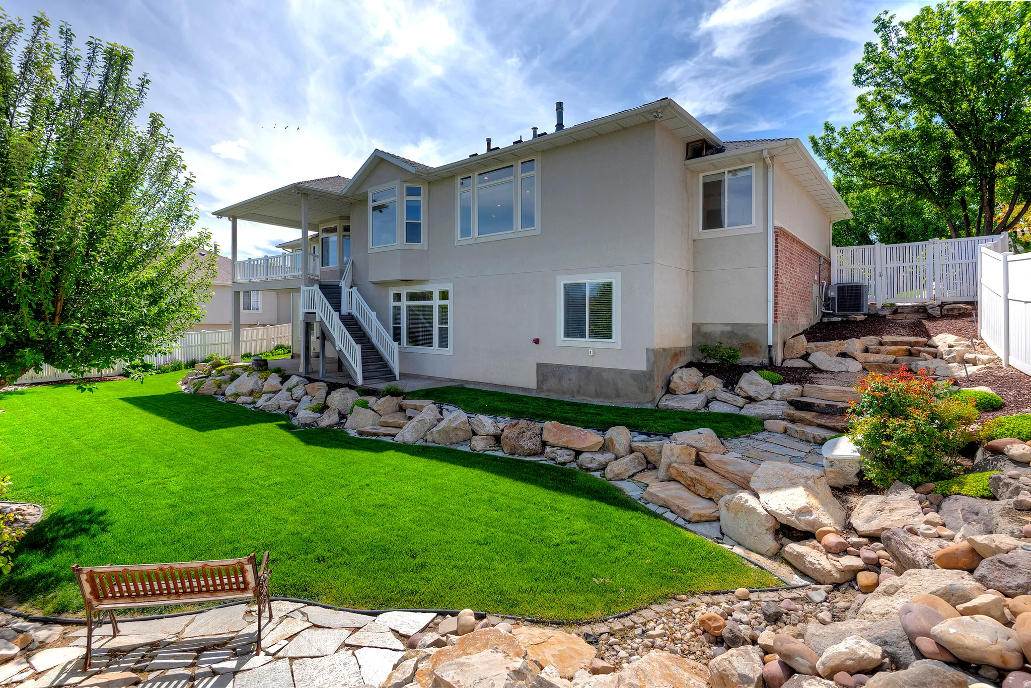 Expansive backyard featuring a manicured lawn, tiered landscaping with natural stone elements, and a white picket fence