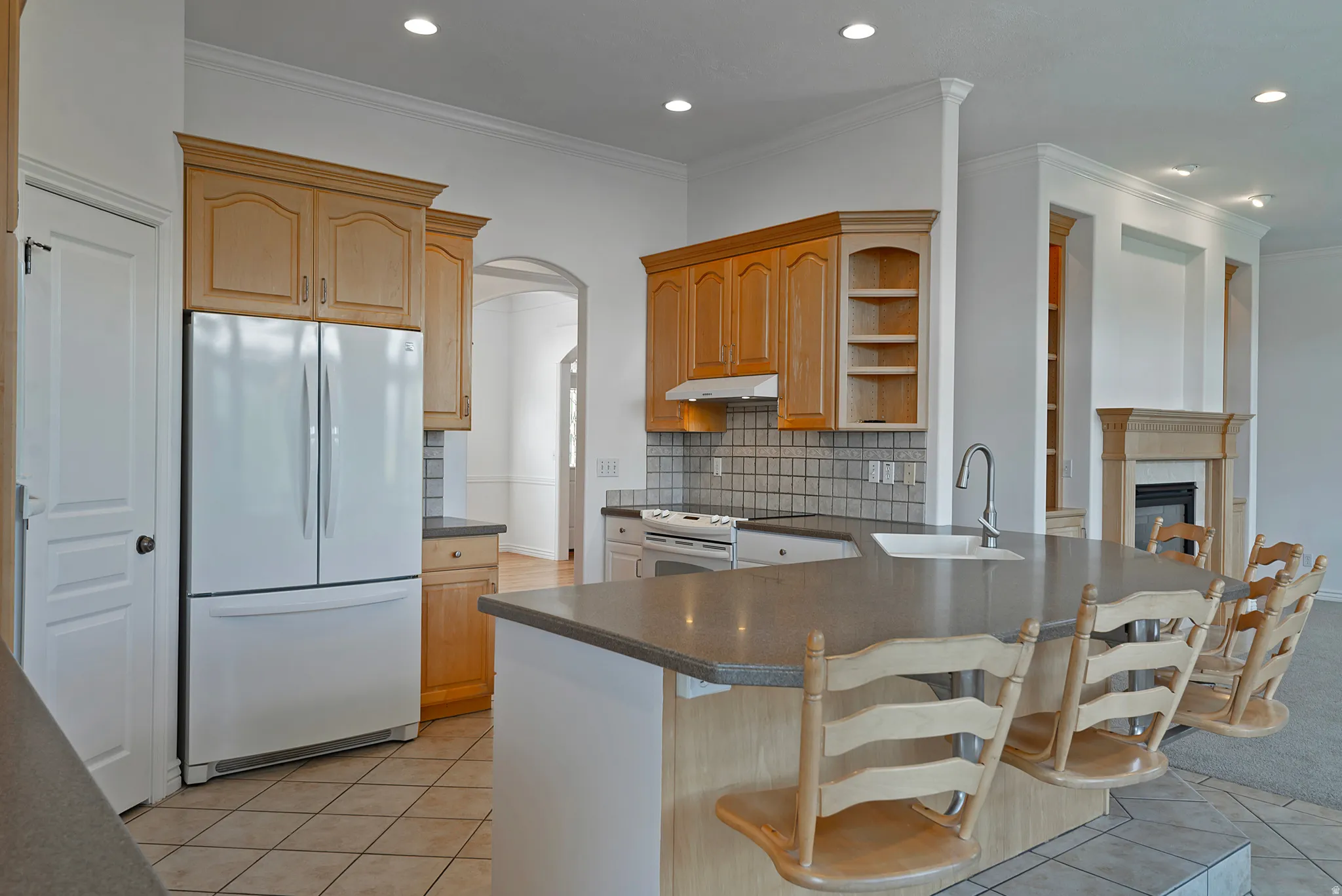 Kitchen featuring wood-finish cabinetry, tile backsplash, and a central island with an integrated sink and breakfast bar