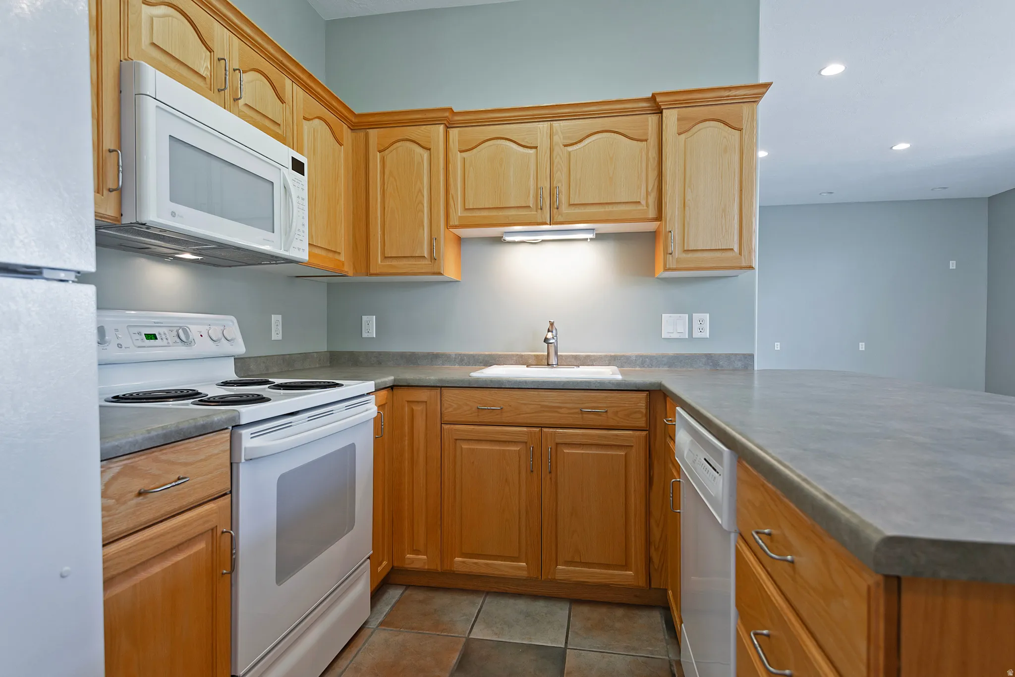 Kitchen featuring light wood cabinetry with brushed nickel hardware, laminate countertops, and a white appliance package including a refrigerator, range, microwave, and dishwasher