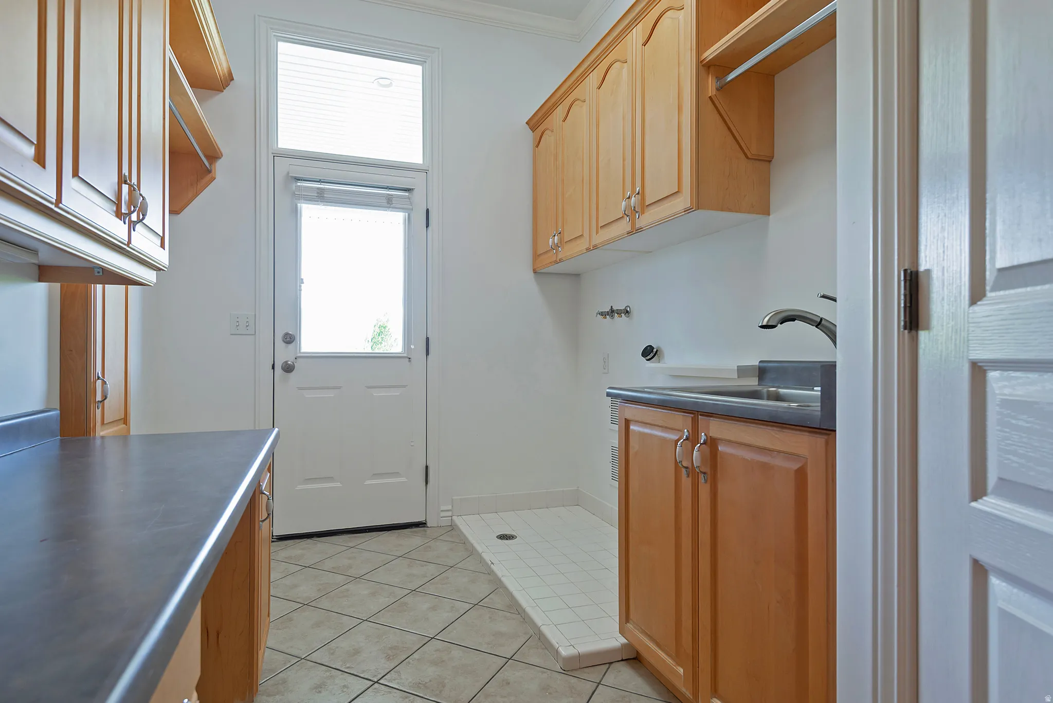 Utility room featuring wood cabinetry, dark countertops, a utility sink, and tile flooring