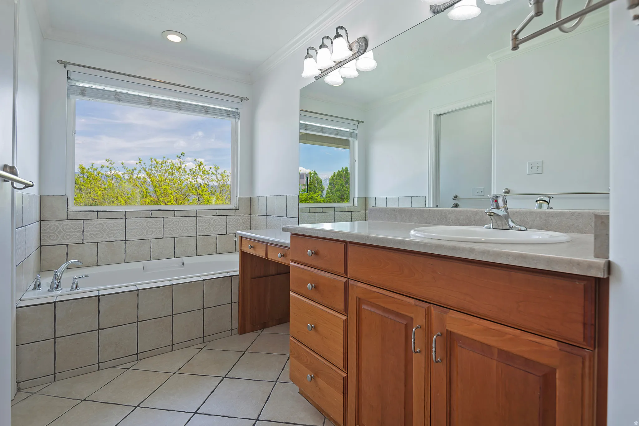 Bathroom featuring a built-in soaking tub with tile surround, a large window, and a vanity with a light-toned countertop and wood-finish cabinetry