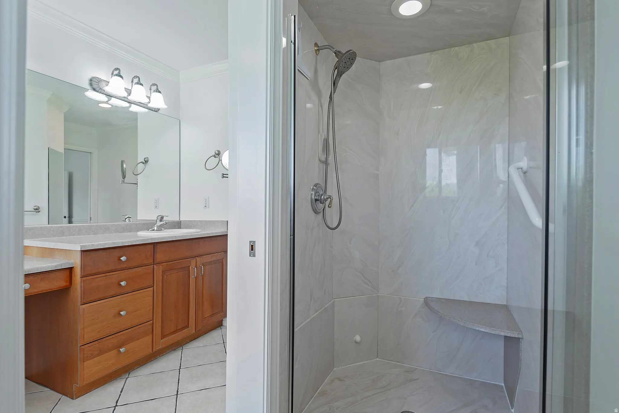 Glass-enclosed shower with white marble-style wall panels, integrated seating bench, and a mounted grab bar