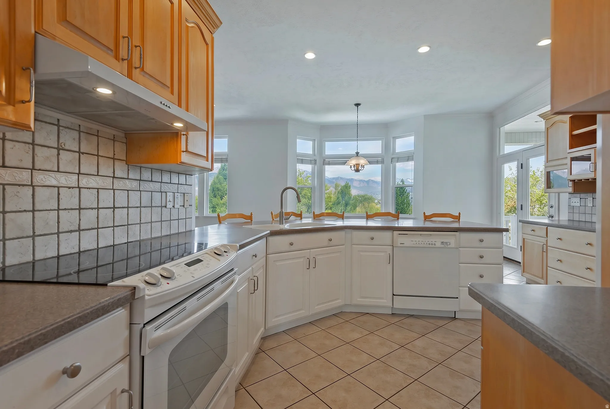 Kitchen featuring light wood-finish cabinetry, white appliances, and a tile backsplash