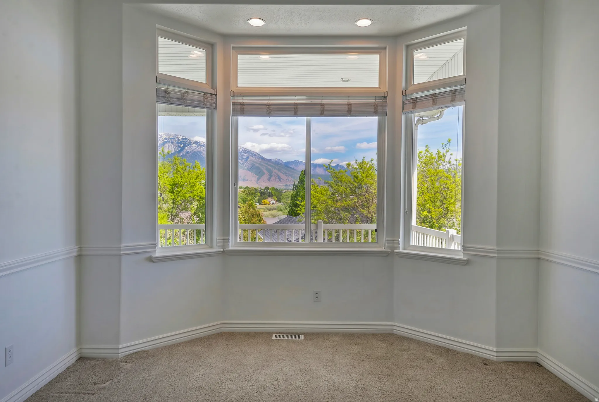Bay window assembly featuring multiple double-hung windows, recessed lighting, white wall paneling, and a mountain backdrop
