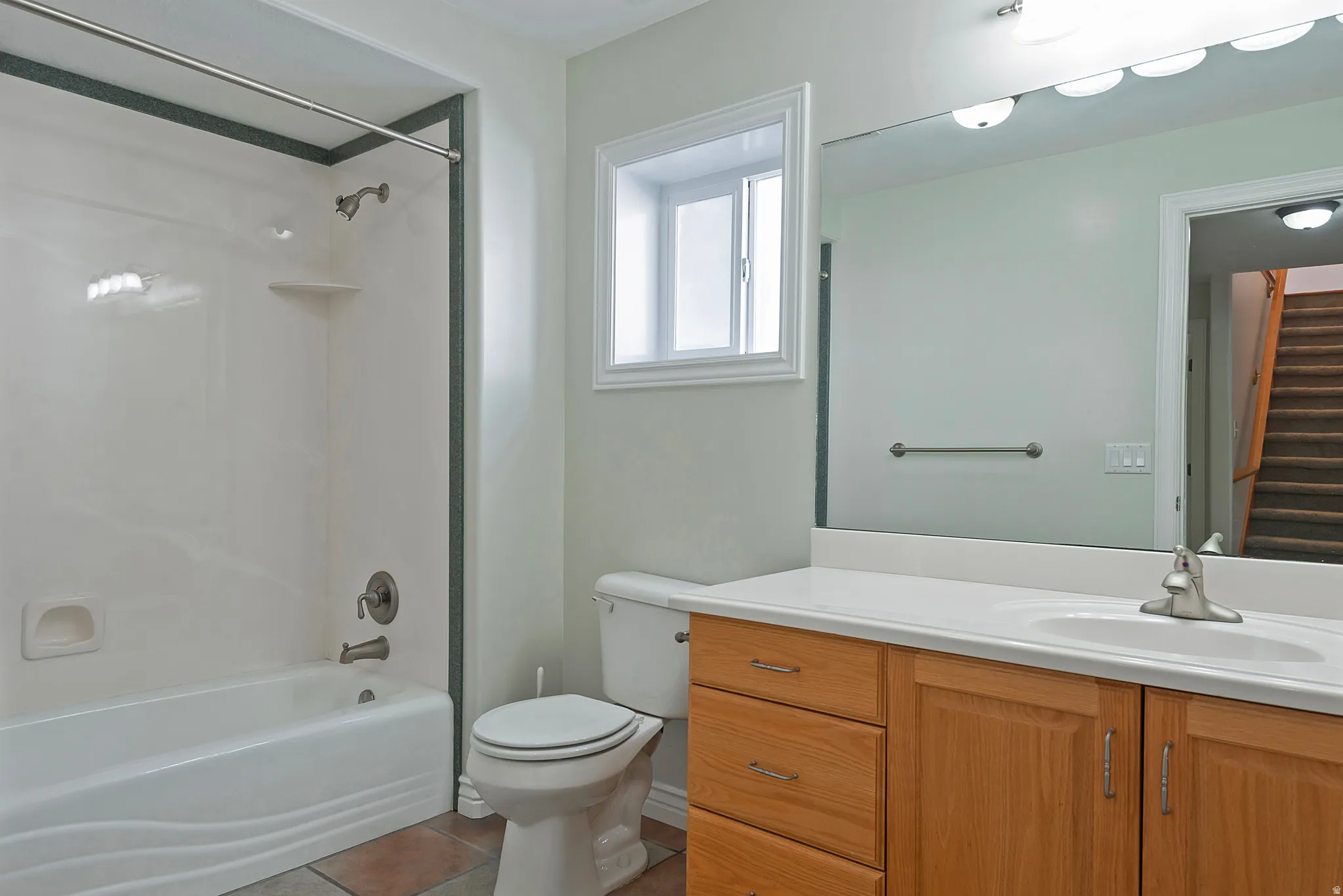 Full bathroom featuring a white tub and shower combination with a single lever faucet, a window with white trim, a wood-finish vanity with a white countertop and integrated sink, and a large wall-mounted mirror
