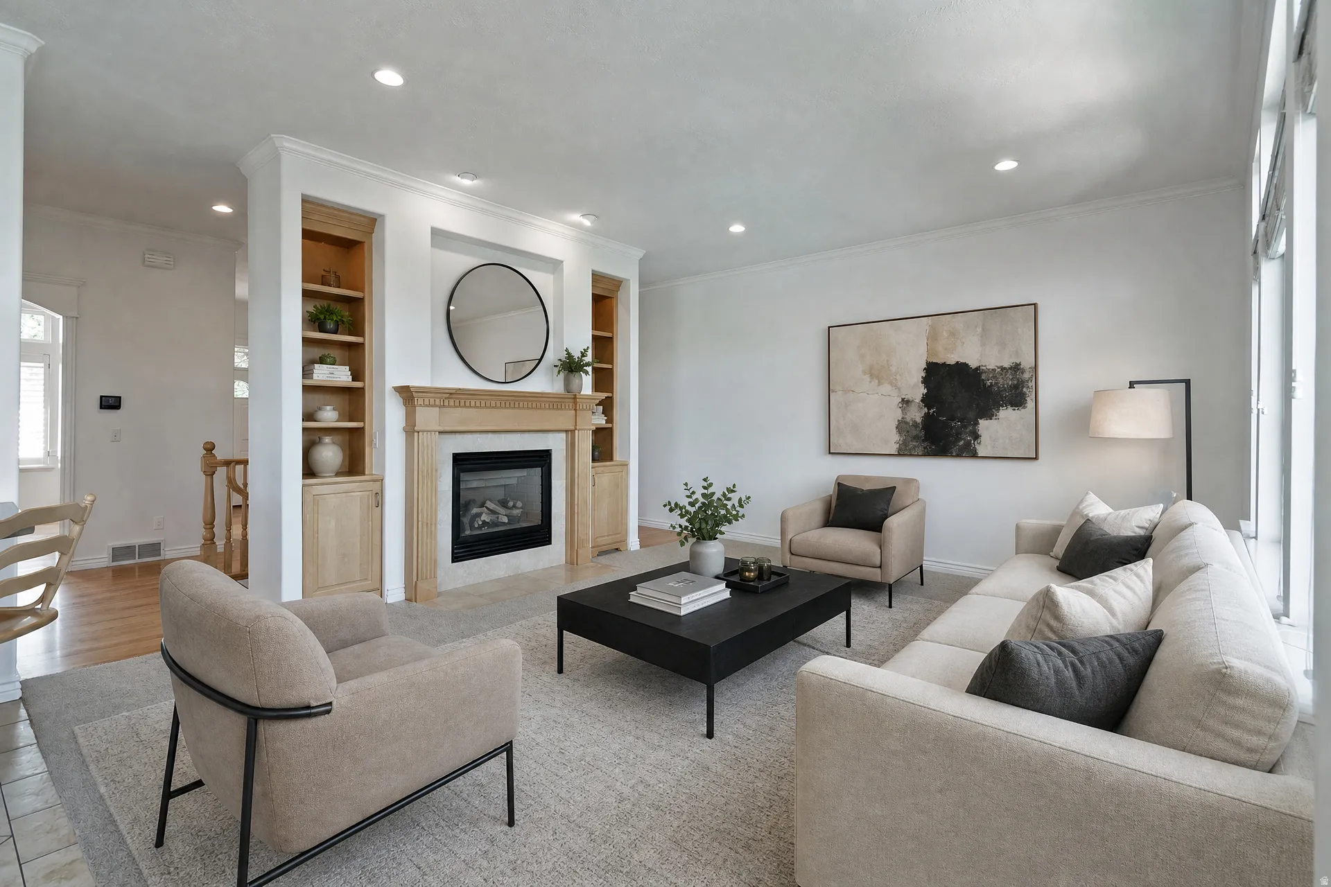 Spacious living area featuring a fireplace with a light wood mantel, recessed lighting, crown molding, built-in shelving, and large windows providing natural light
