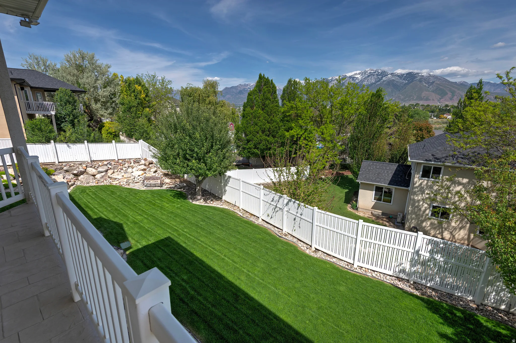 Expansive backyard featuring a manicured lawn, white vinyl fencing, and mature trees