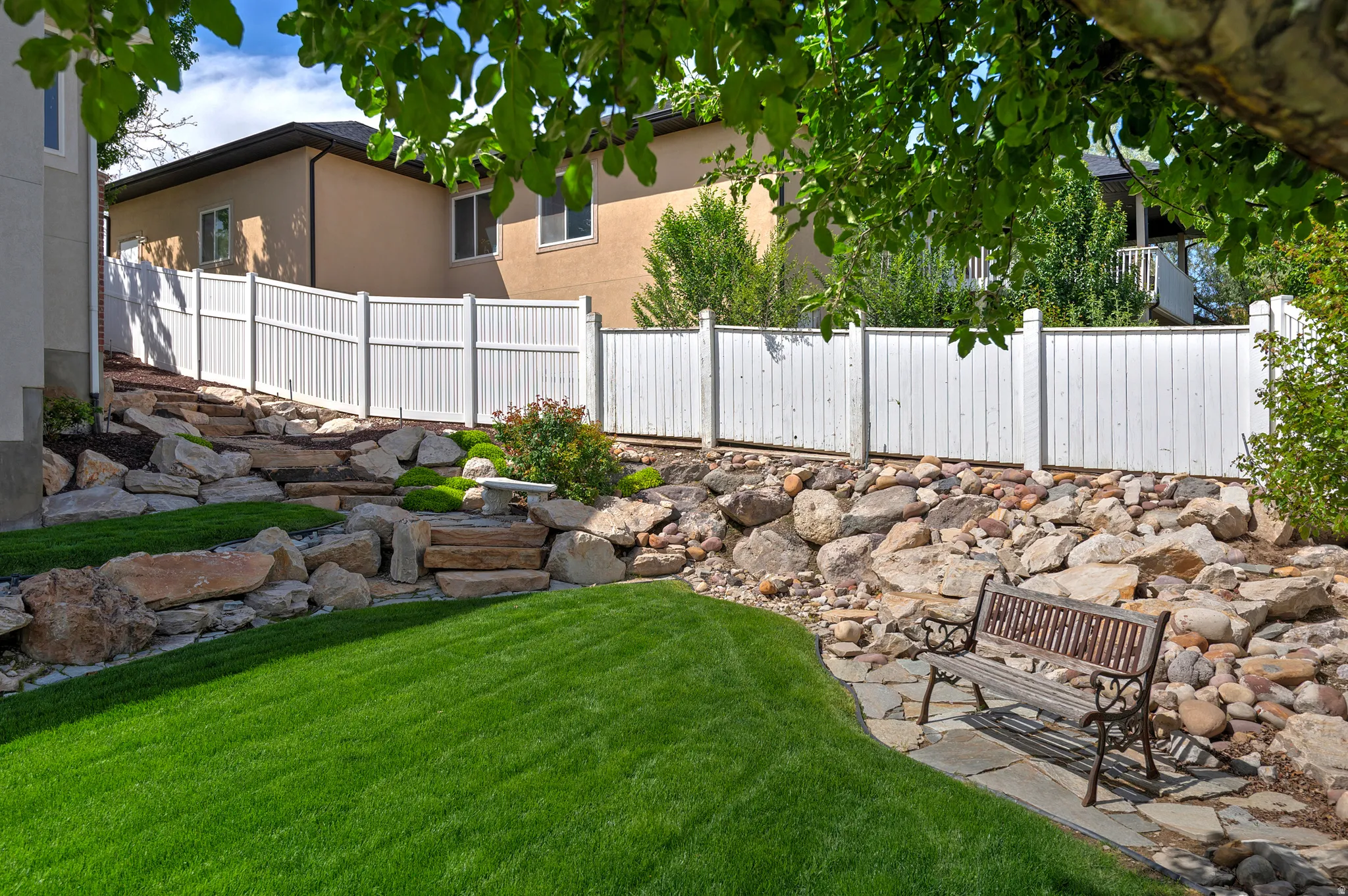 Tiered backyard landscaping featuring a manicured lawn, stone hardscaping, and a white privacy fence