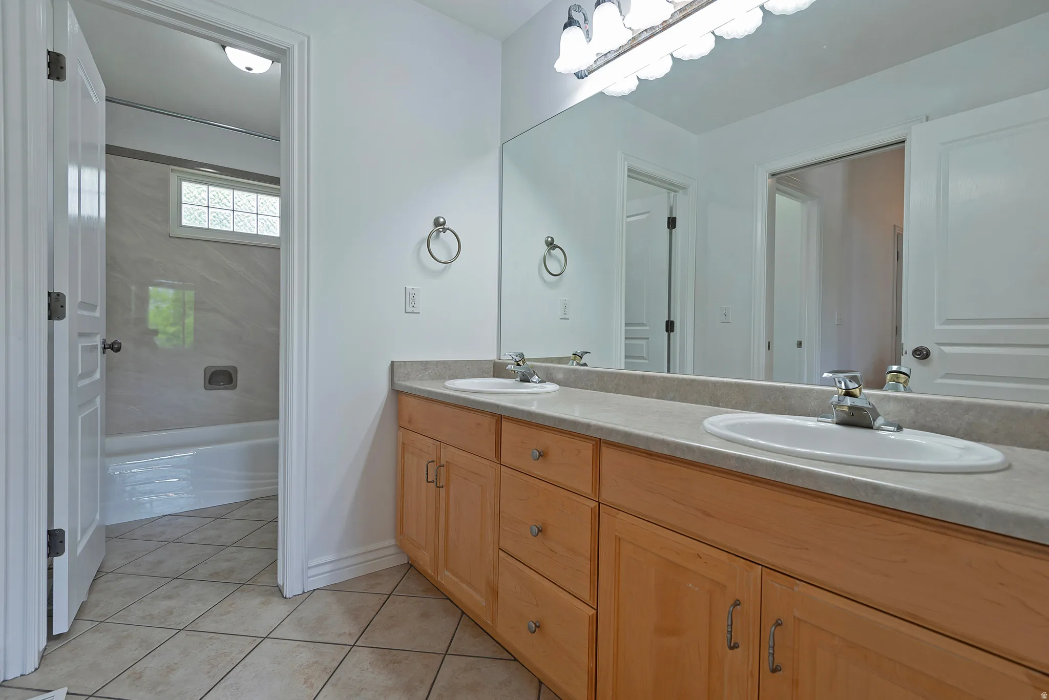 Double vanity with light wood cabinetry, white oval sinks, and a full-width mirror