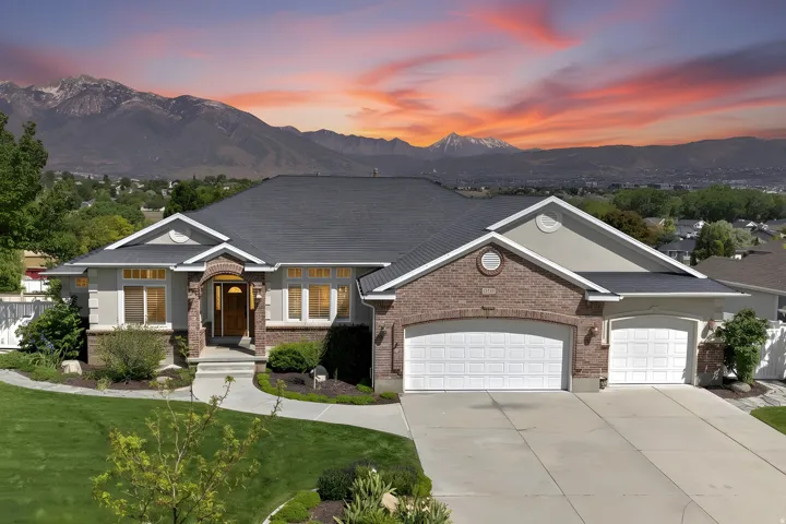 Exterior featuring brick and stucco accents, a dark shingle roof, arched entryway, and a multi-car garage