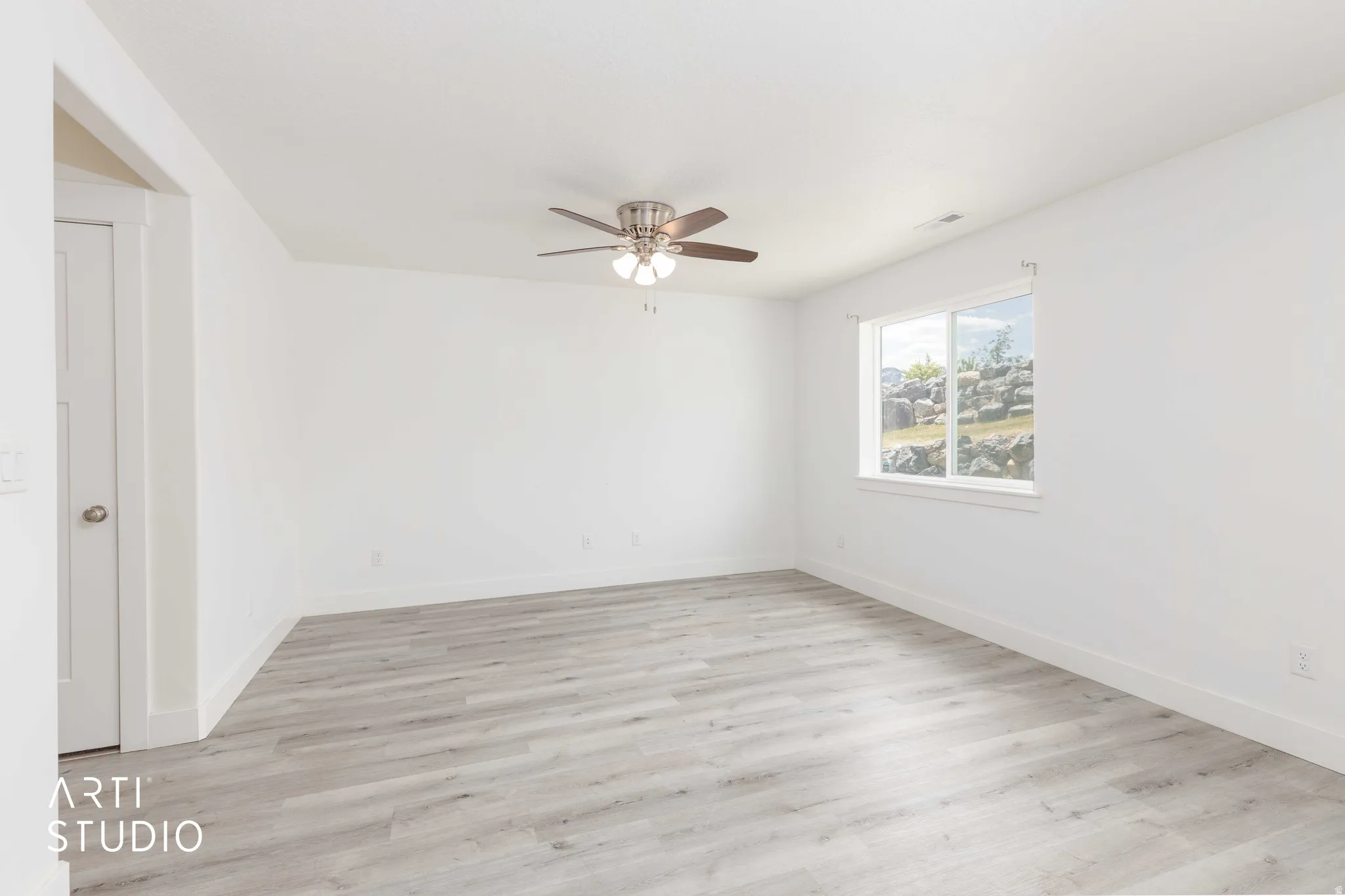 Spacious room featuring light wood-finish flooring, white walls, and a ceiling fan with integrated lighting