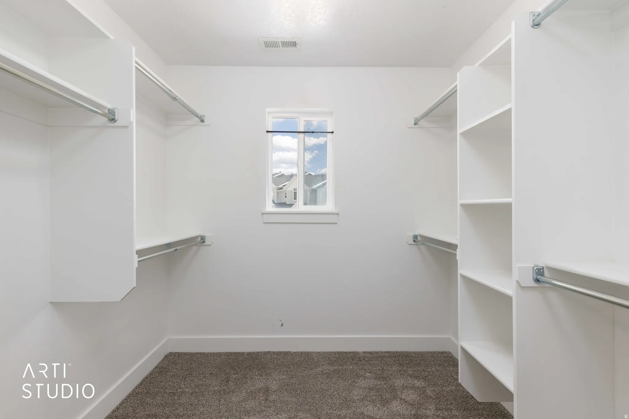 Spacious walk-in closet featuring built-in shelving, multiple hanging rods, and a window for natural illumination