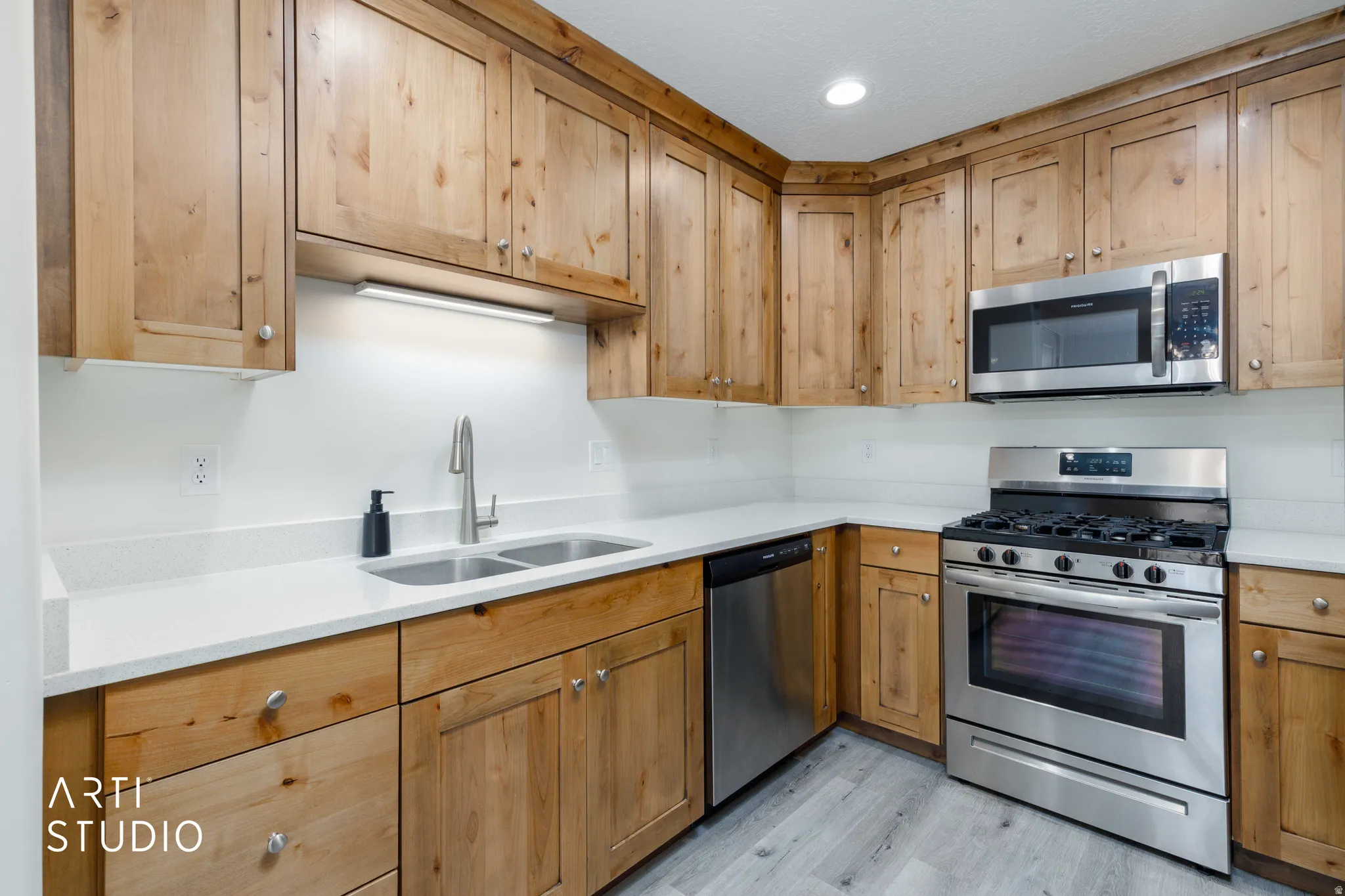 L-shaped kitchen featuring wood cabinetry, light countertops, stainless steel appliances, and wood-finish flooring