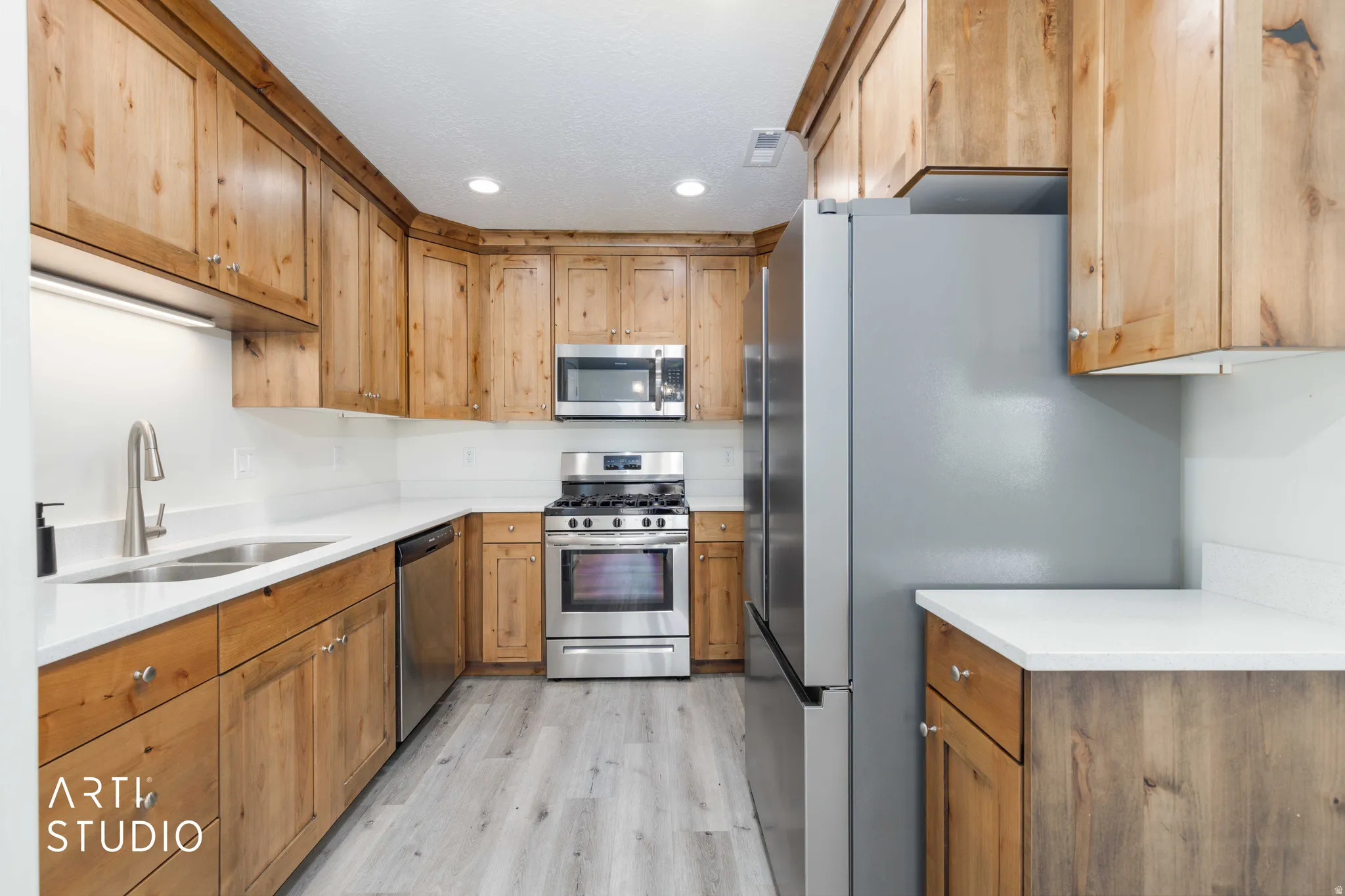 Kitchen featuring natural wood cabinetry, white countertops, stainless steel appliances, and wood-finish flooring