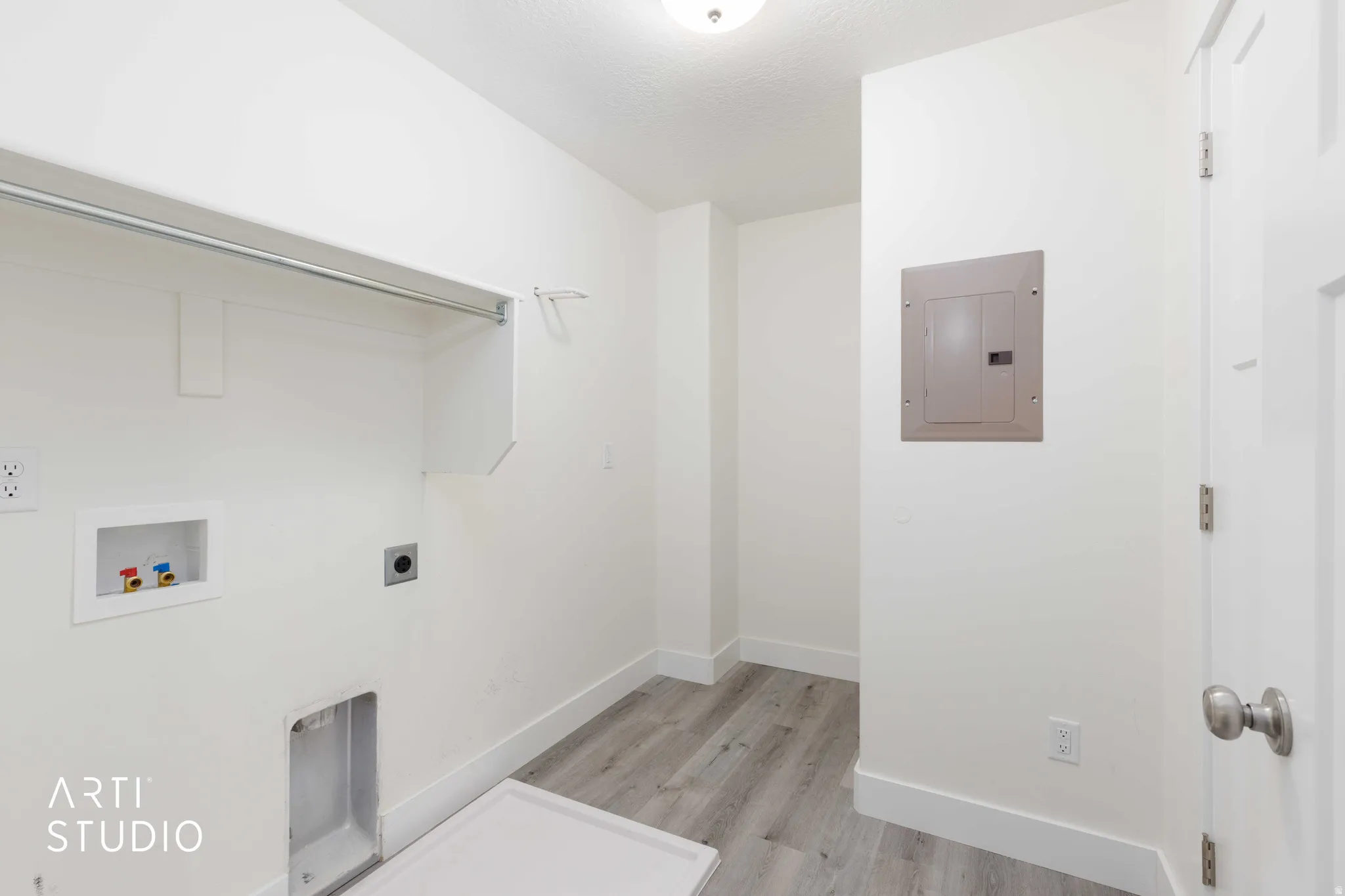 Dedicated laundry space featuring wood-finish flooring, white walls, and a built-in hanging rod