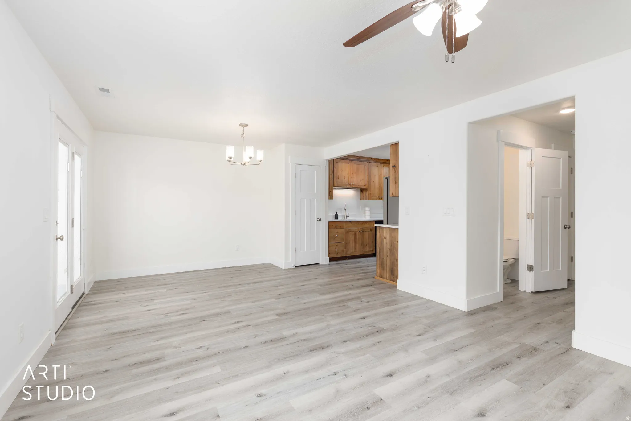 Open-concept living space featuring wood-finish flooring, white walls, and a contemporary chandelier