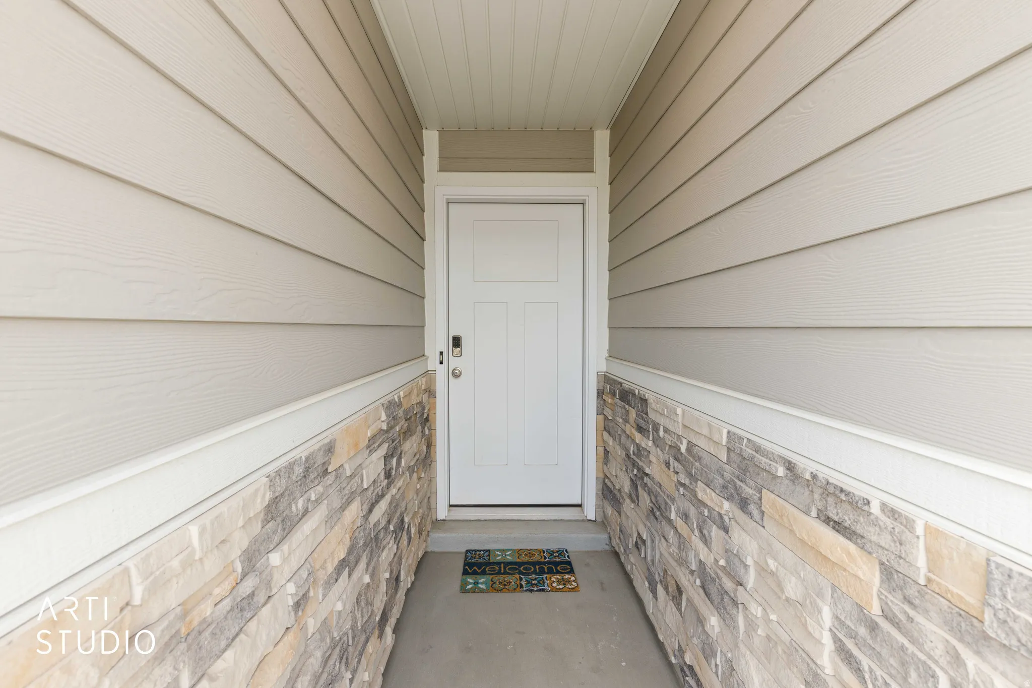 Covered entryway featuring a white panel door, horizontal siding, and a stacked stone veneer accent