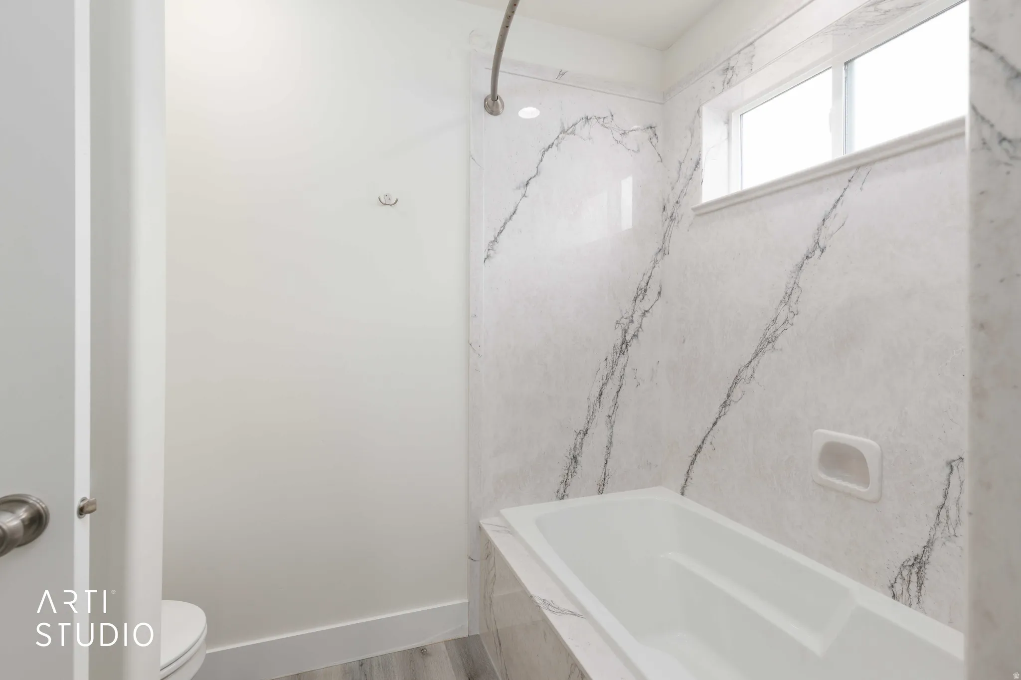 Bathtub with a marble-patterned surround, recessed shower niche, and an integrated window