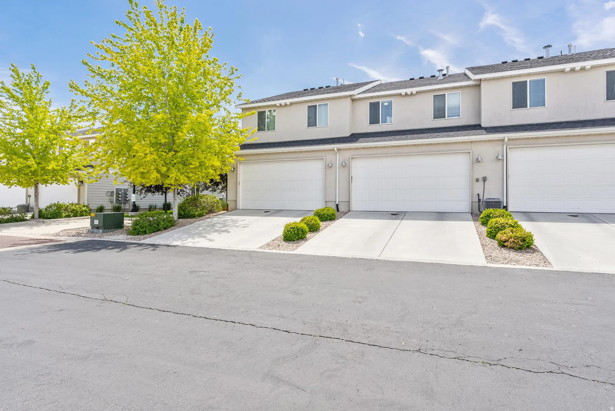 Contemporary townhome-style residences featuring light-toned stucco exteriors and dark shingle roofing