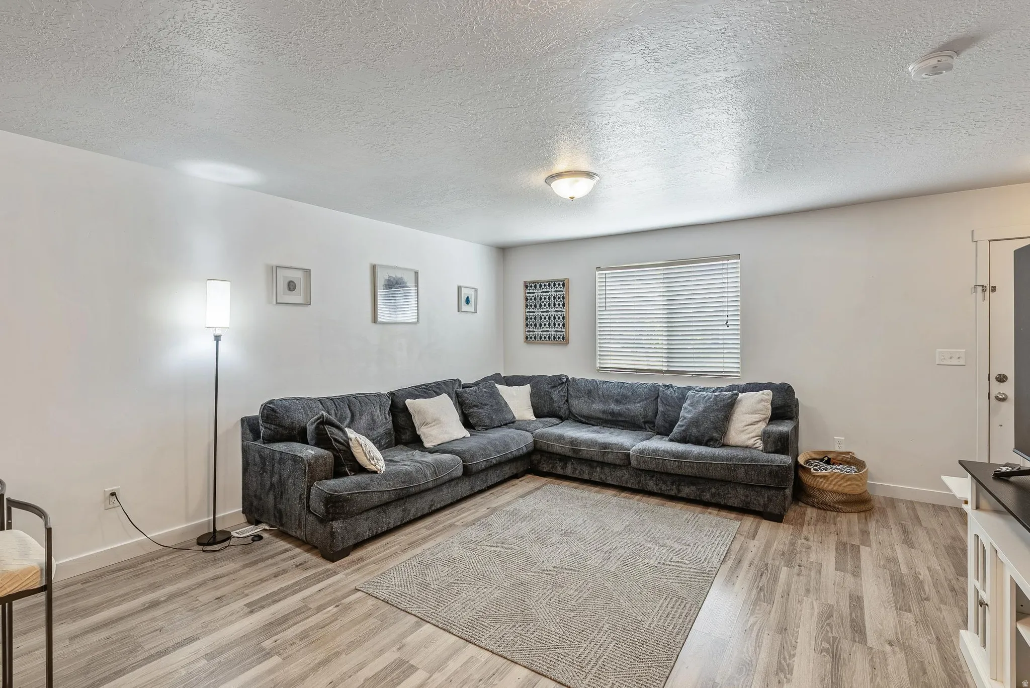 Living area featuring light wood-finish flooring, white walls, and a recessed window with blinds