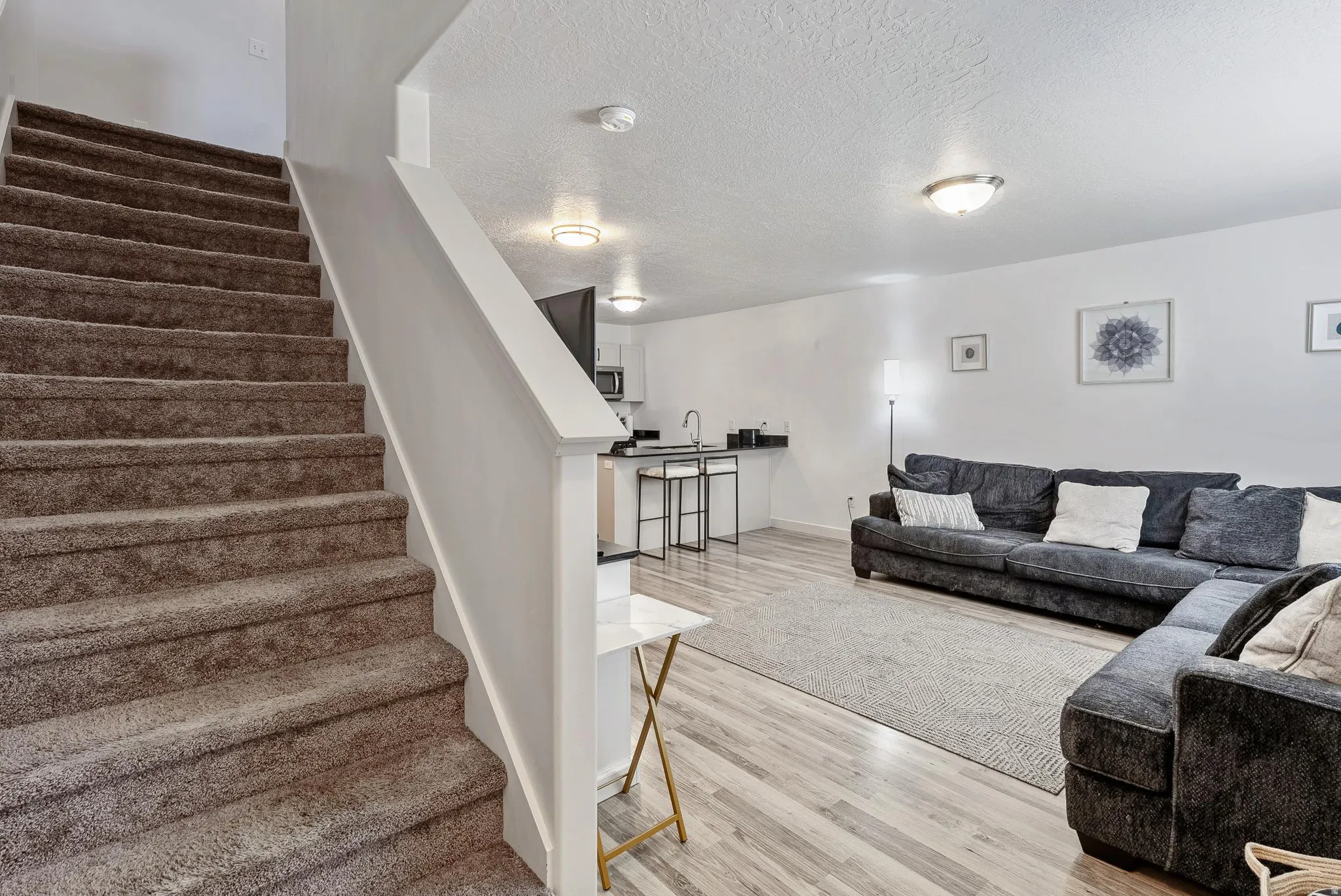 Lower-level living area with light wood-finish flooring, a neutral area rug, and white walls
