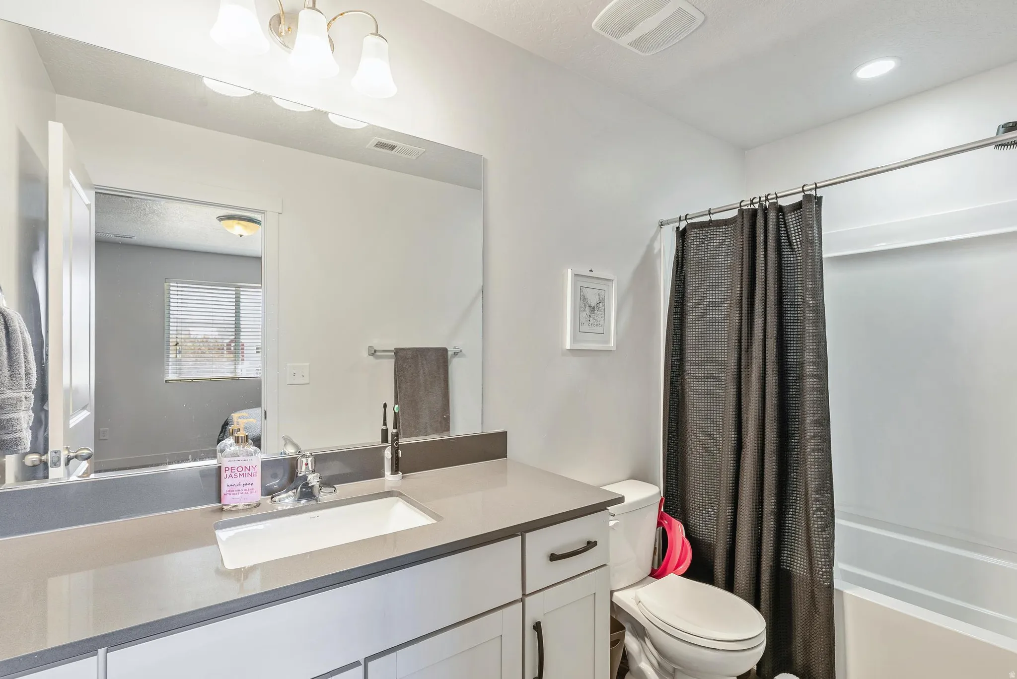 Bathroom featuring a white vanity with an undermount sink, a large wall-mounted mirror, and a built-in shower-over-tub combination