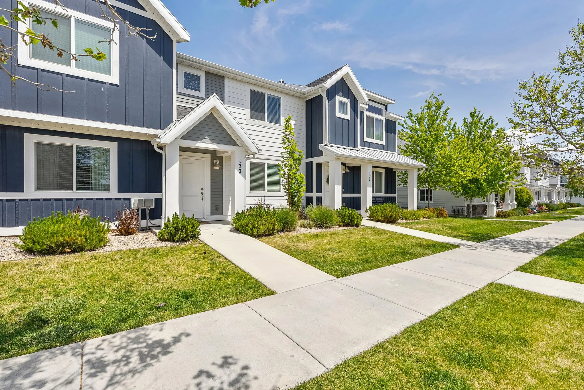 Modern townhome exterior featuring contrasting dark blue and white siding, a covered entry, and a well-maintained lawn